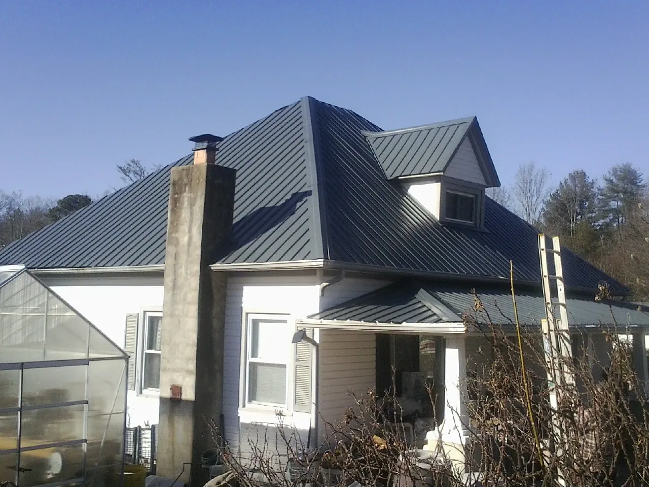 Dark blue standing seam metal roof on a white farmhouse with dormer — Slate & Tile Roof Repair by Roofing Brothers in Desoto