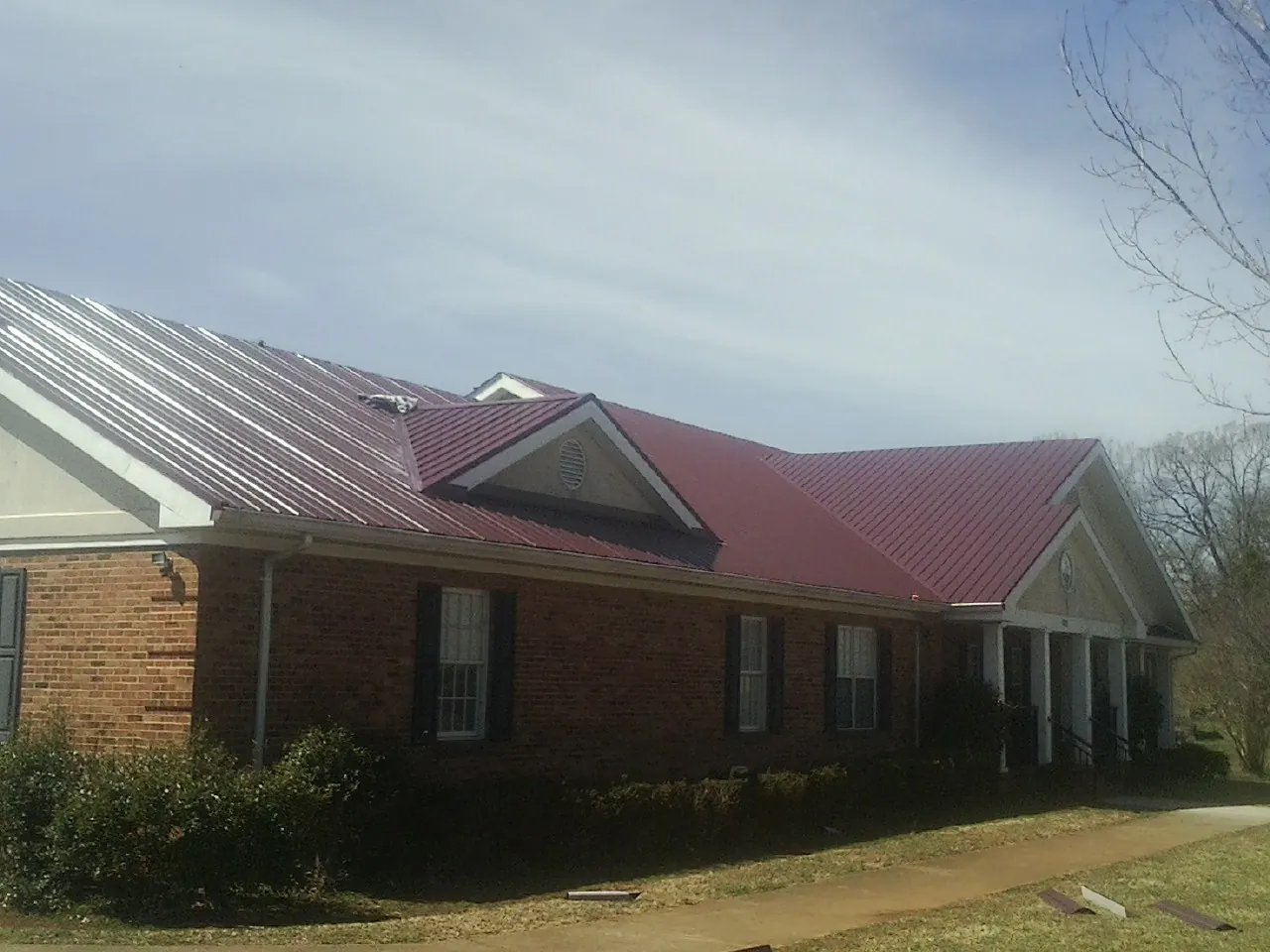 Red metal roof with gabled entries on a long brick building, from a Hail Damage Roof Repair job in Desoto