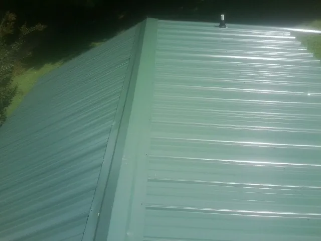 New green metal panels meeting at the ridge of a roof — Flat Roof Repair work by our crew in Desoto