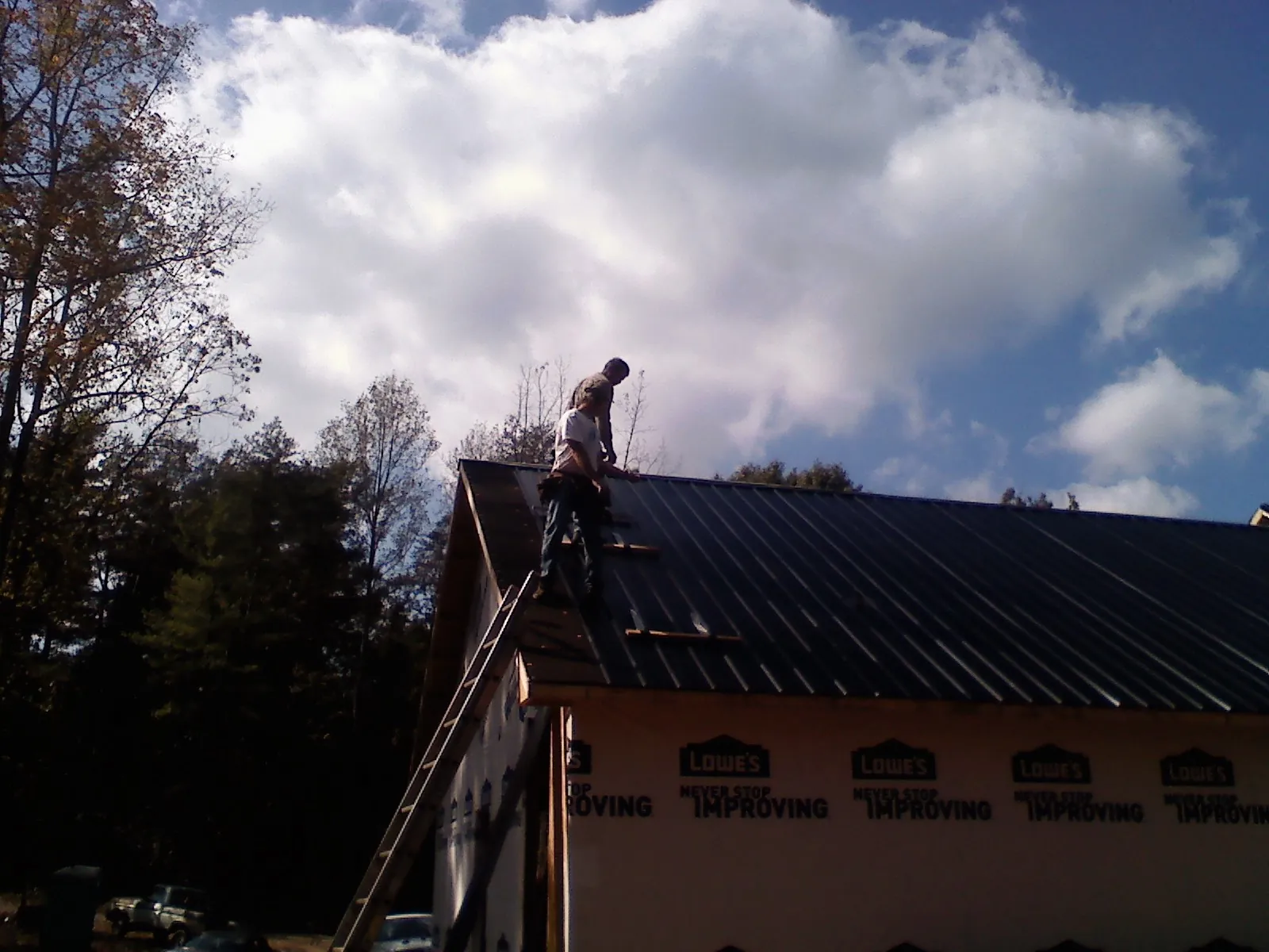 Roofer fastening dark metal panels high against a cloudy sky, from a Roof Inspection job in Desoto